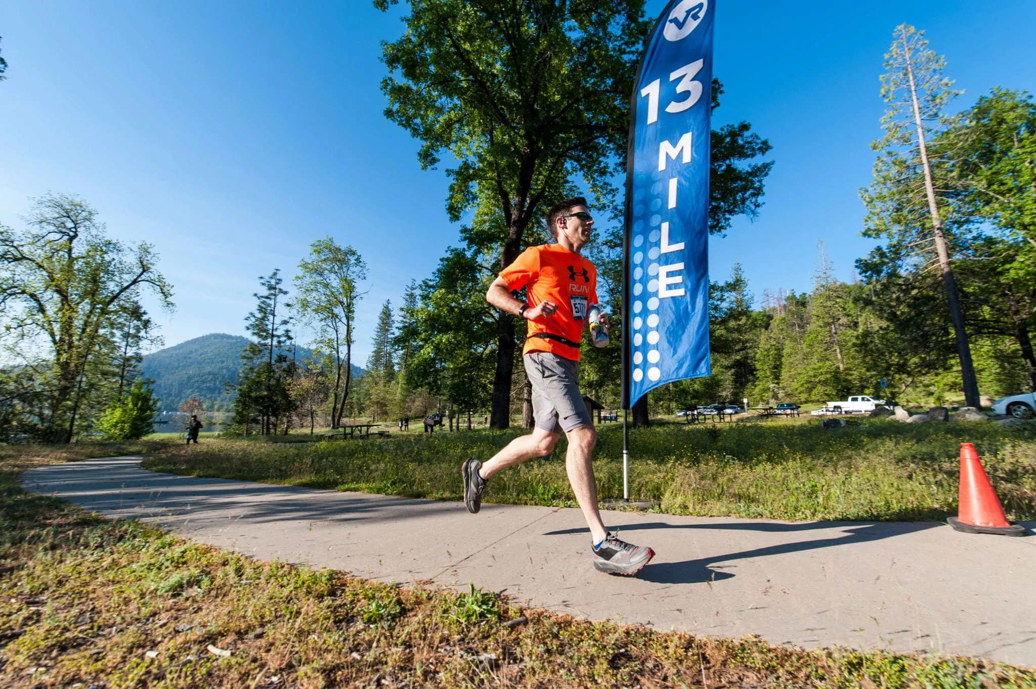 2019 Yosemite_LUC0205 Adult running past a flag that says Mile 13 with trees and a lake behind him