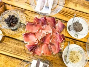 A plate of cured meat with olives and table settings