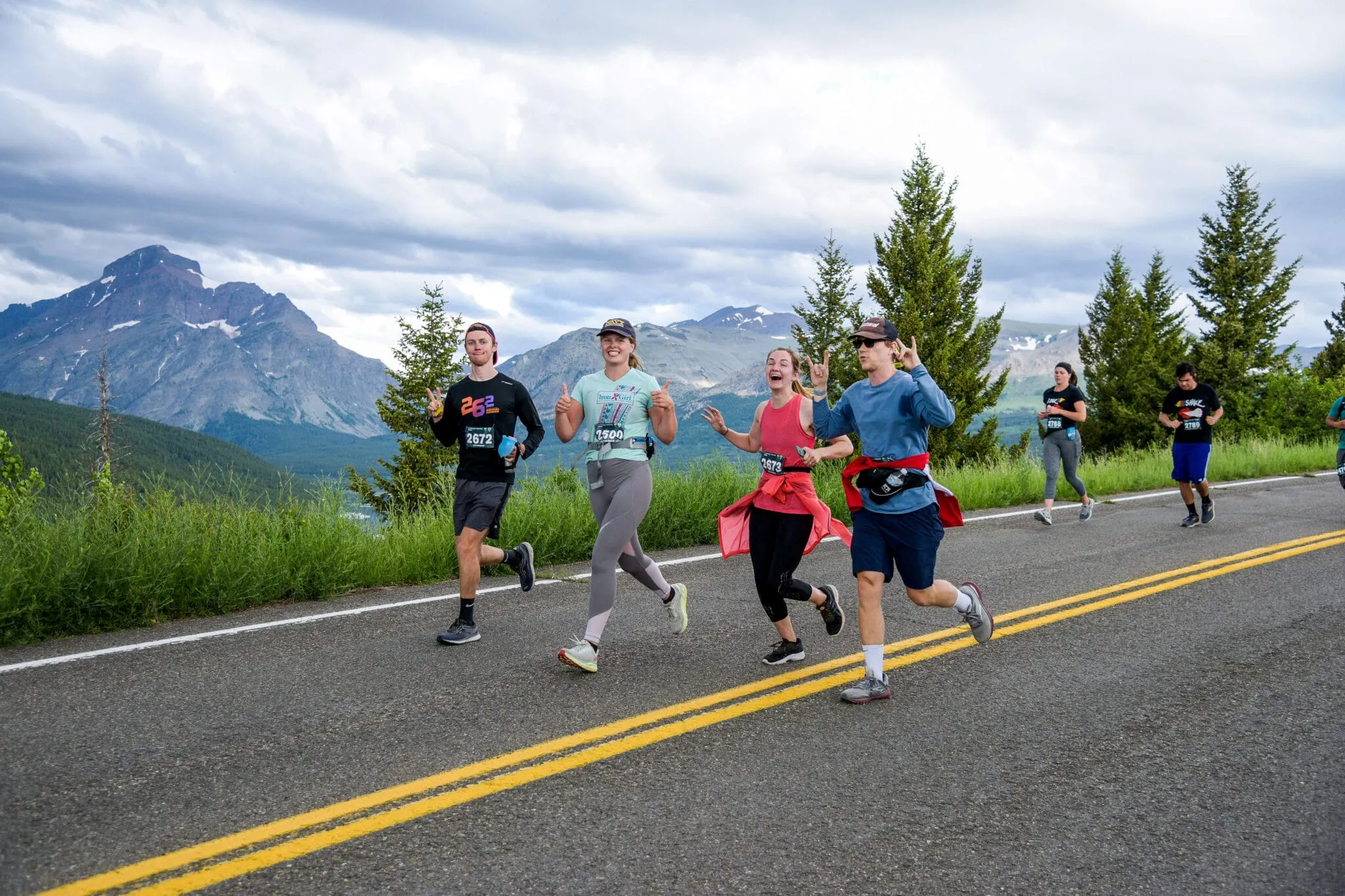 A group of people running on a road with Two Medicine's mountains behind.